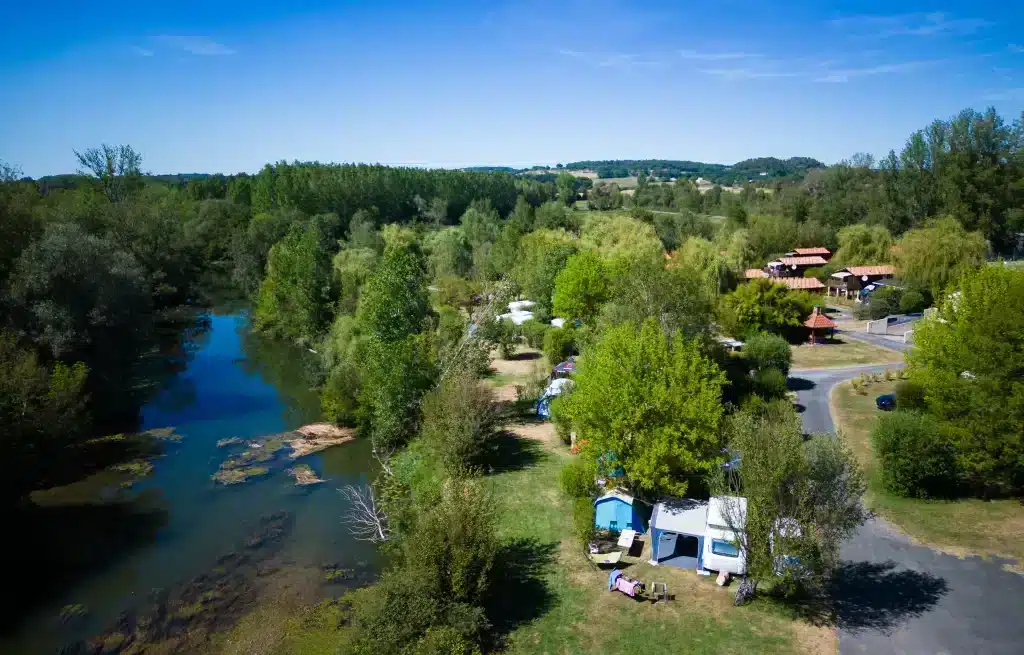 Vue aérienne d'un camping près d'une rivière verdoyante.